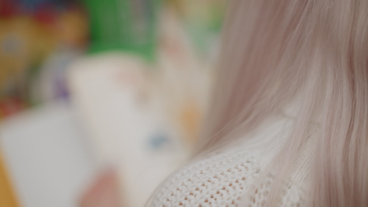aerial view of woman with long hair flipping pages of illustrated children textbook in bright store aisle, motion blur capturing dynamic page turning, showcasing manicure and watch
