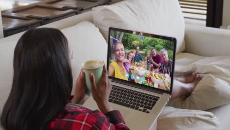 Afroamerikanische-Frau-Hält-Eine-Kaffeetasse-In-Der-Hand-Und-Führt-Einen-Videoanruf-Auf-Dem-Laptop,-Der-Zu-Hause-Auf-Der-Couch-Sitzt