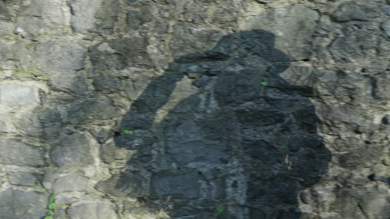 la sombra de una mujer que camina sobre un muro de piedra poniéndose un sombrero
