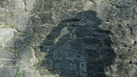 Walking-woman's-shadow-on-stone-wall-putting-on-hat