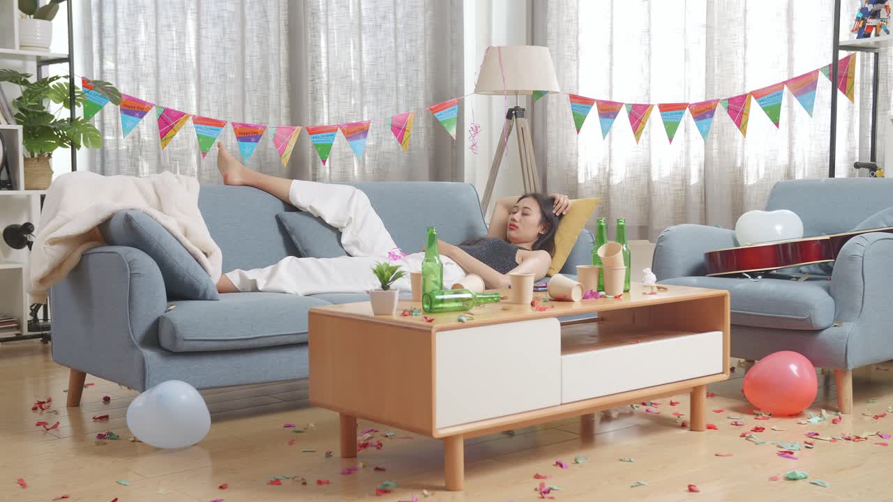 술에 취한 아시아 여성이 집에서 파티를 축하한 후 소파에서 잠을 자고 있습니다.