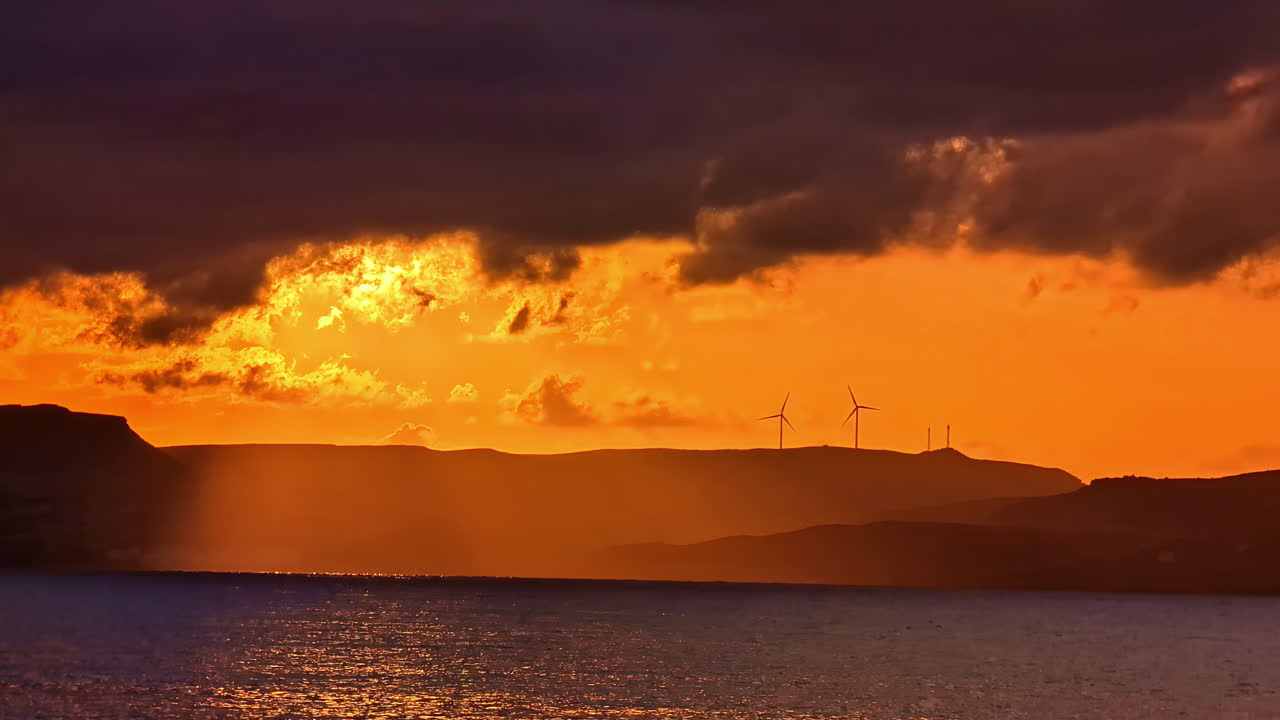 Wind Turbines Over Mountains With Fiery Sunset Sky. Wide Shot
