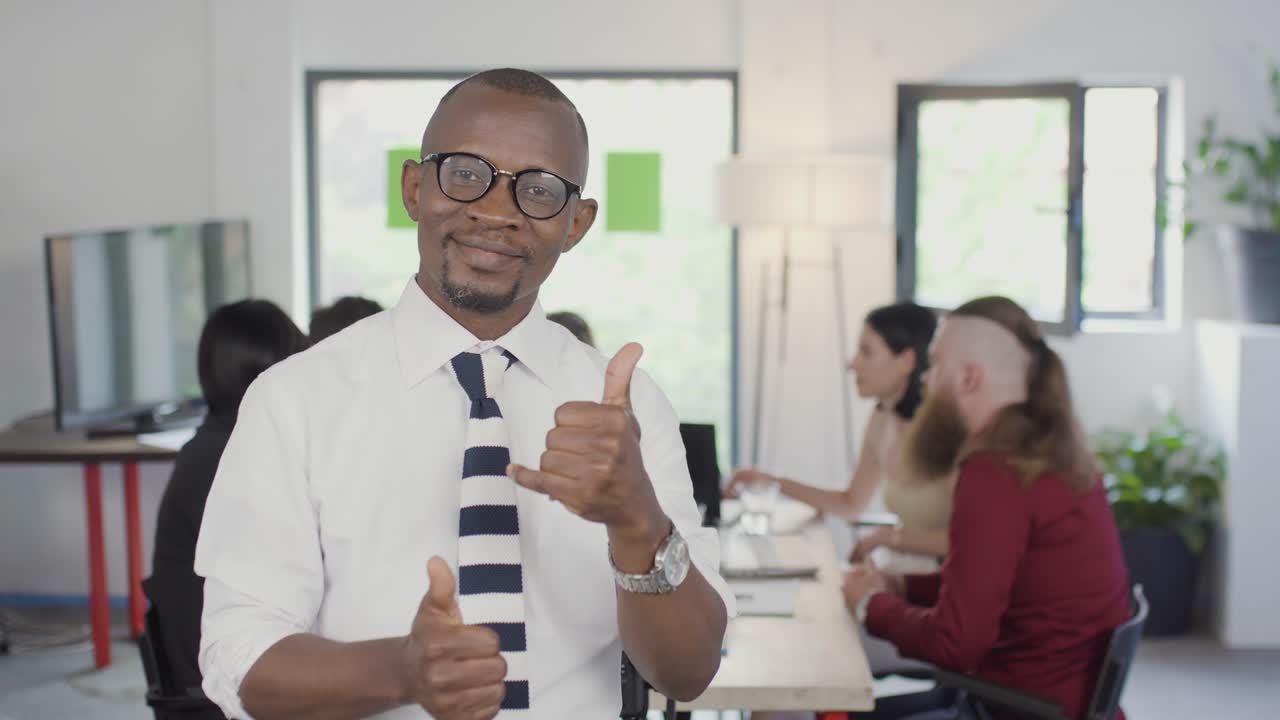 Confident African American businessman portrait. Happy successful man posing with his multiethnic colleagues brainstorming in a meeting. Making like gesture and giving applause.