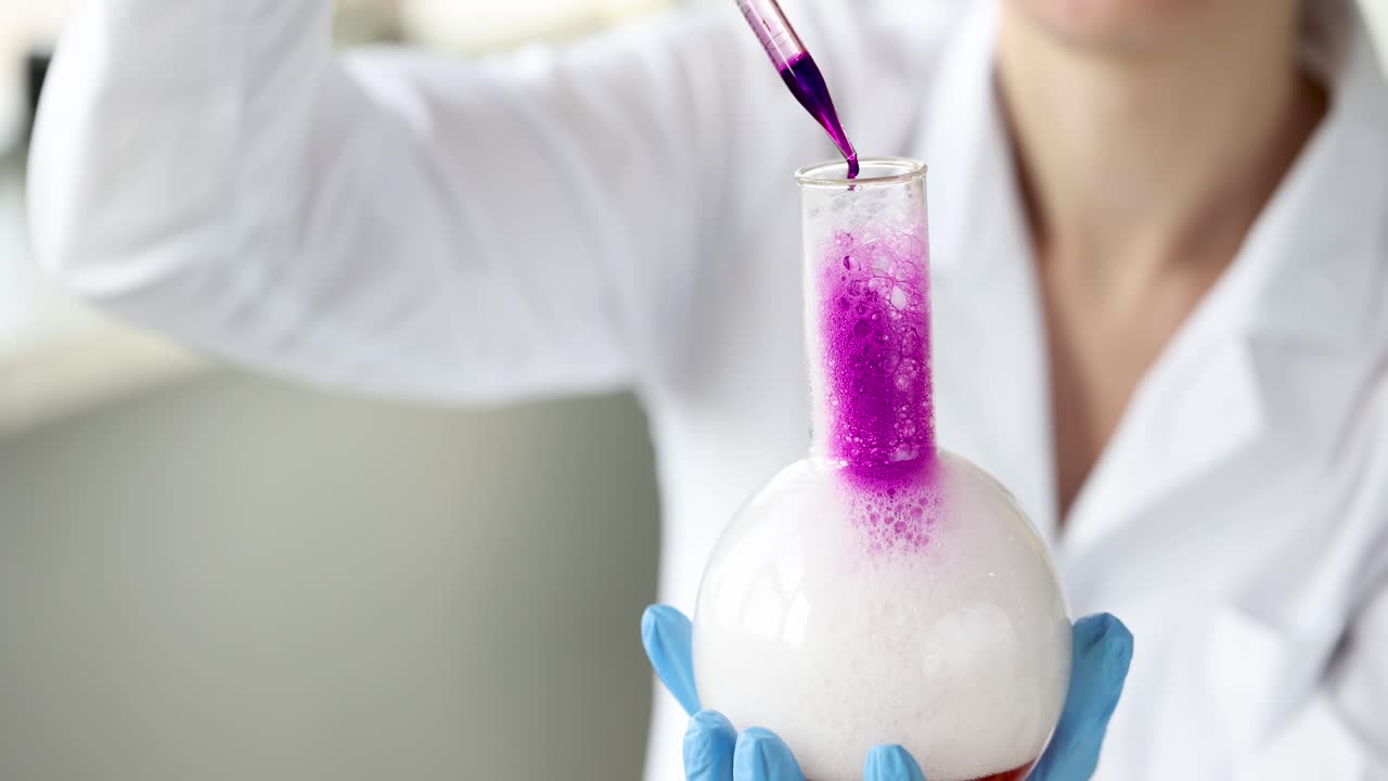 Scienziato chimico che fa cadere liquido rosa in reagente con pipetta, filmato 4k