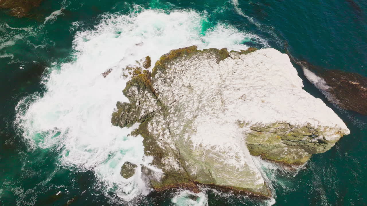 White foamy waves of aquamarine water splashing by the rock covered with salt. Brown algae accumulation on top of the ocean at California coast. Top view.