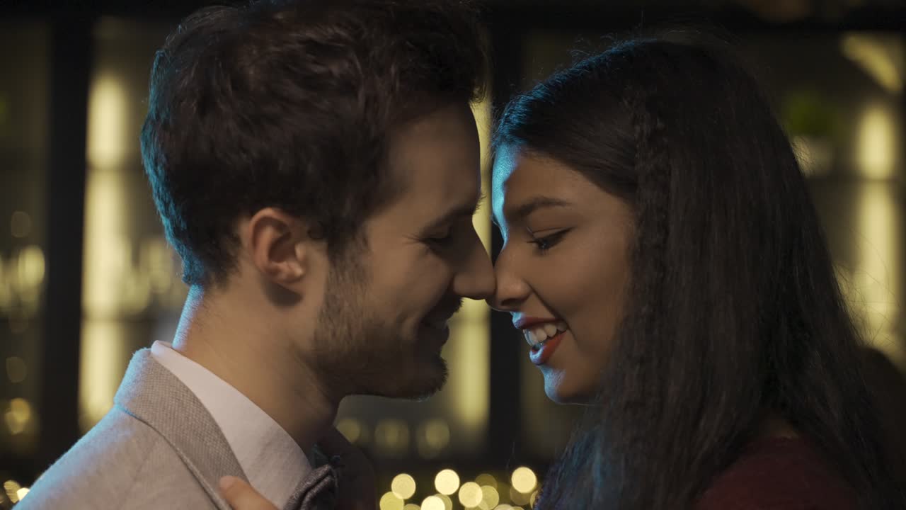 Close-up view of a couple celebrating New Year's Eve party, they get closer and kiss while smiling