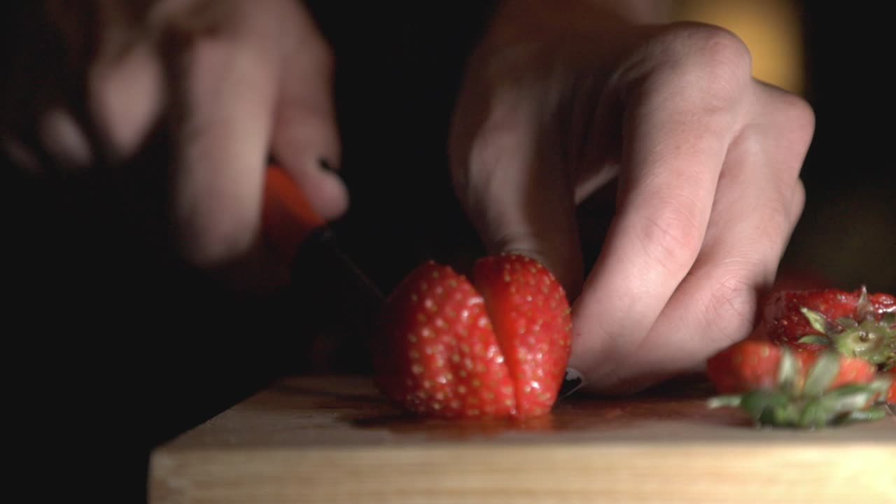 Cutting Strawberry Into Two Using Small Kitchen Knife On Chopping Board. - Close up shot