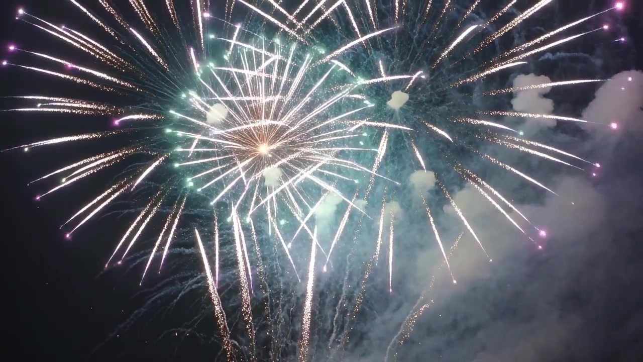 Lancio di fuochi d'artificio aerei che salgono ed esplodono di notte per uno spettacolo pubblico, lasciando fumo magenta.