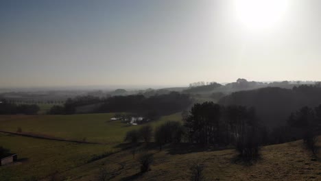 Aerial-view-of-beautiful-green-hills-with-trees-and-lakes,-moving-toward-the-sunset-in-Odsherred,-Denmark