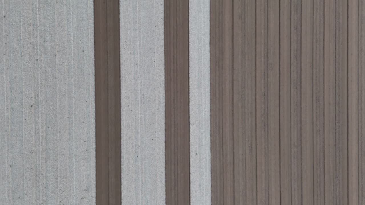 Perpendicular overhead drone shot of alternating pale and dark furrows stretching across tilled field