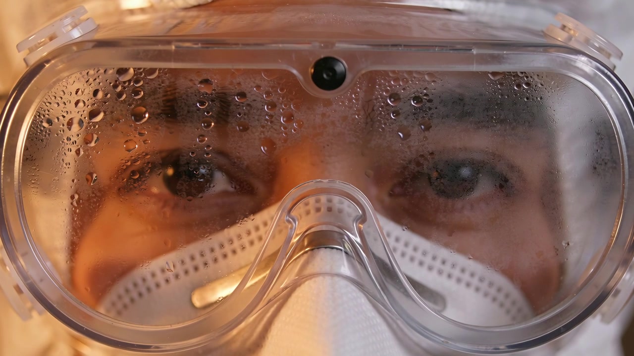 Breathing male clinician wearing PPE and N95 mask in lab, exhaling condensation fogging goggles