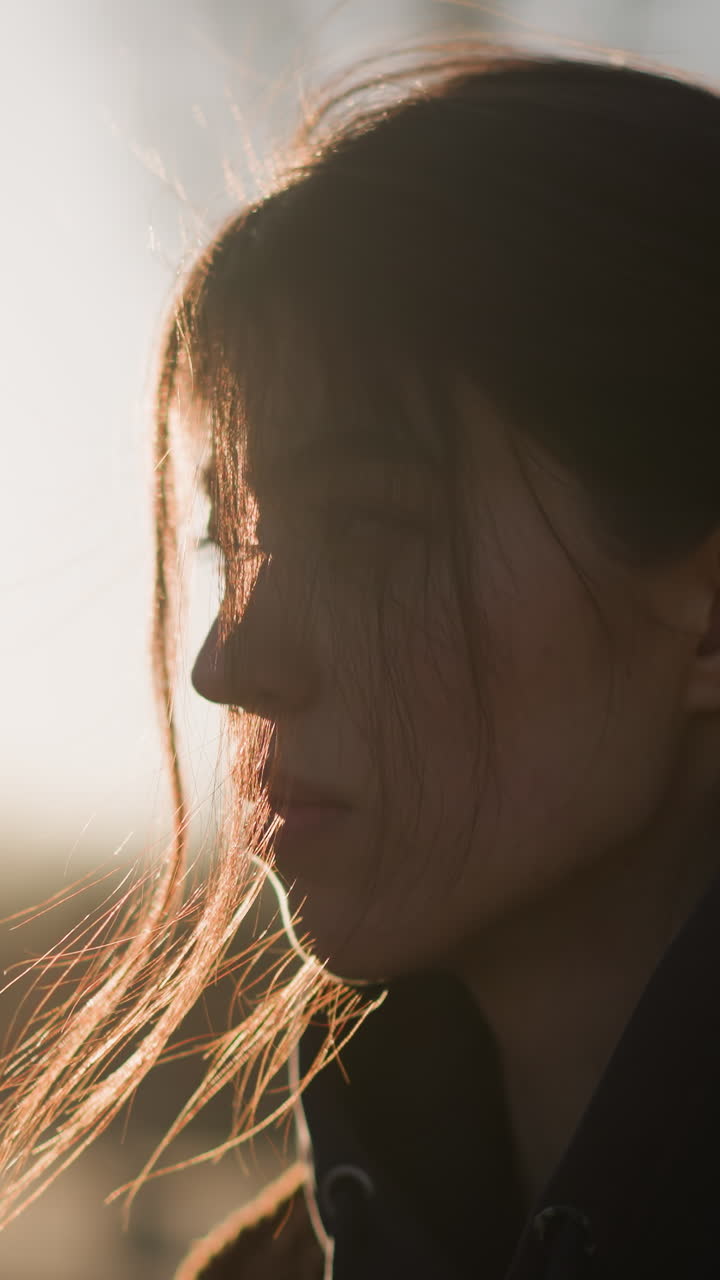 una chica caminando con el corazón pesado, su cabello cubriendo parcialmente su cara. el suave resplandor de la puesta de sol en el fondo agrega un estado de ánimo sombrío y reflexivo, momento de introspección y melancolía