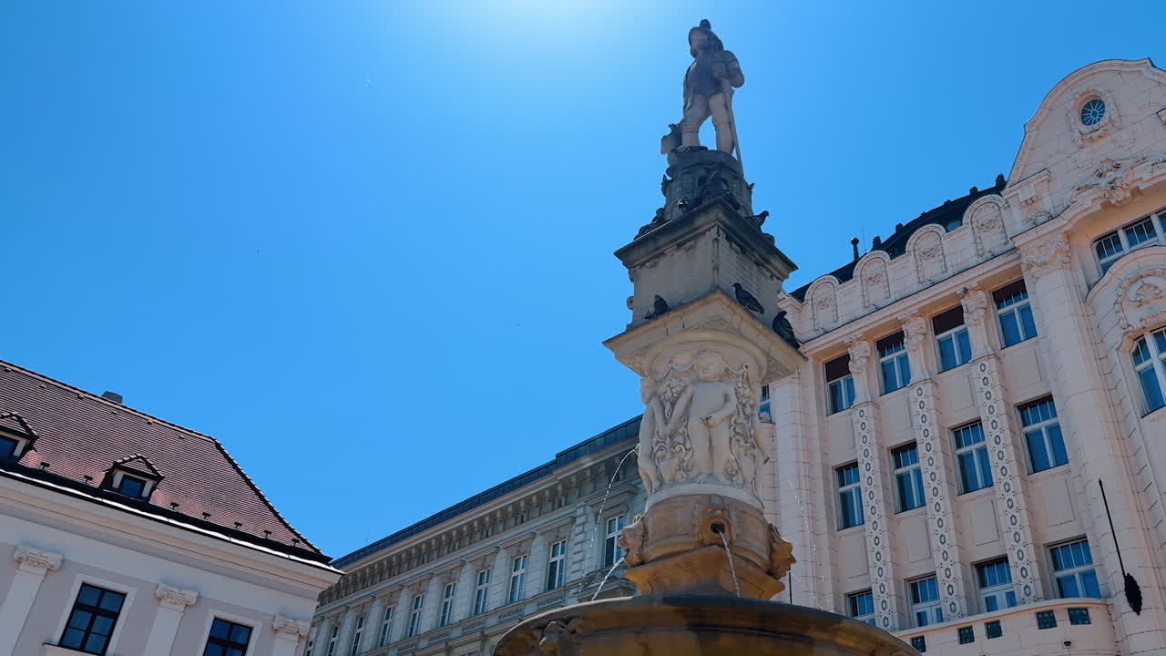 Column of the fountain with a statue on top. Pigeons sit on the fountain. Low angle view. Bratislava, Slovakia