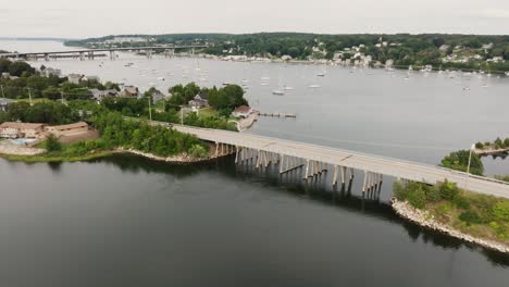 Aerial-view-of-coastal-town-flying-over-bridge-to-see-sail-boats-in-harbor-in-New-England