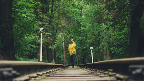 mädchen in einem gelben regenmantel, das auf der eisenbahn spaziert und sich der kamera nähert