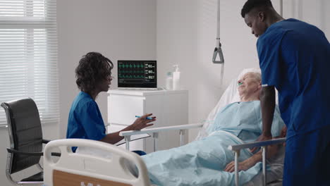 a team of african ethnic group doctors a man and a woman talk to an elderly male patient. a doctor and a nurse talk to a bedridden patient in a hospital ward