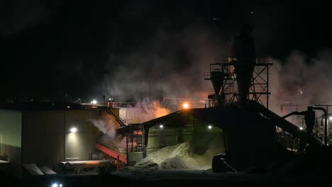 una mirada nocturna a un silo de aserrín rodeado de humo industrial