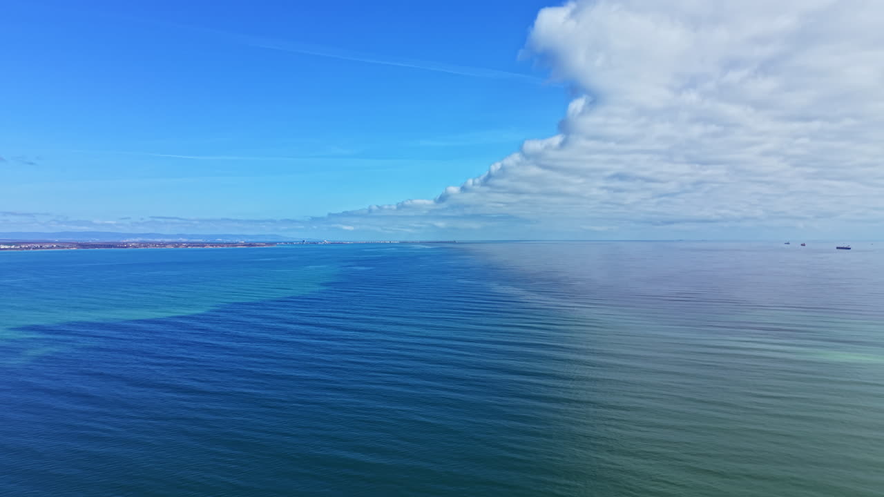 Paesaggio marino con acqua limpida e blu, onde calme, navi lontane e nuvole nel cielo sopra l'oceano durante il giorno.