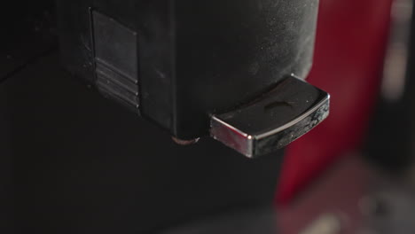 close-up shot of espresso machine nozzle dispensing a small amount of coffee into a paper cup. a person's hand is slightly visible, holding the cup as the coffee is being poured