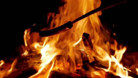 Hot-dog-sausage-on-a-stick-being-prepared-over-open-camping-fire