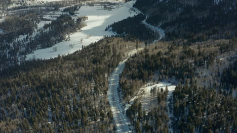Aerial-following-truck-down-rural-mountain-road-towards-small-town-in-winter