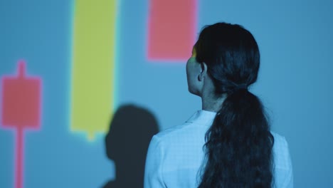 mujer visitando una exposición de arte inmersivo con proyección de formas y patrones en la pared 2