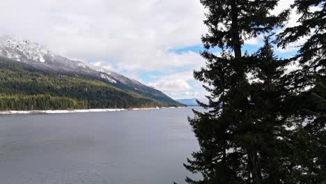 Forward-shot-through-evergreen-trees-revealing-Lake-Kachess-in-Washington-State-on-a-partly-cloudy-day