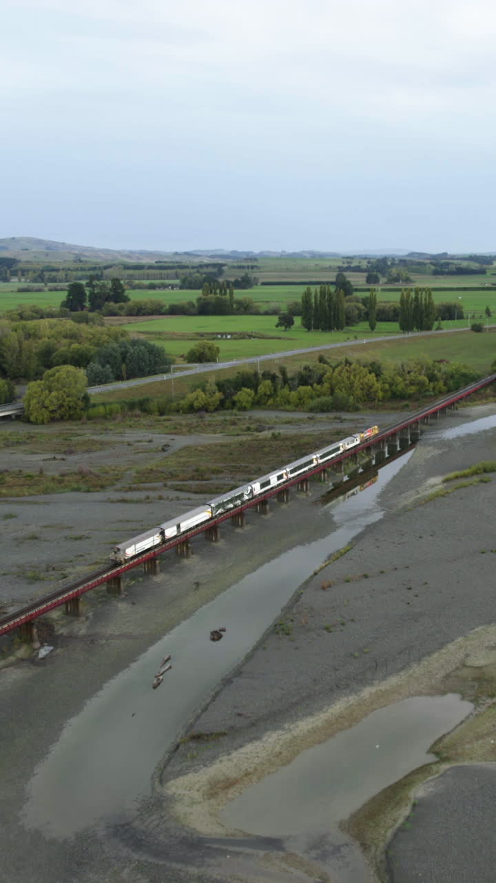 Vertical drone shot following a train crossing a bridge on the Waiau river in NZ