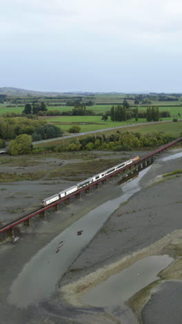 vertical drone shot following a train crossing a bridge on the waiau river in nz