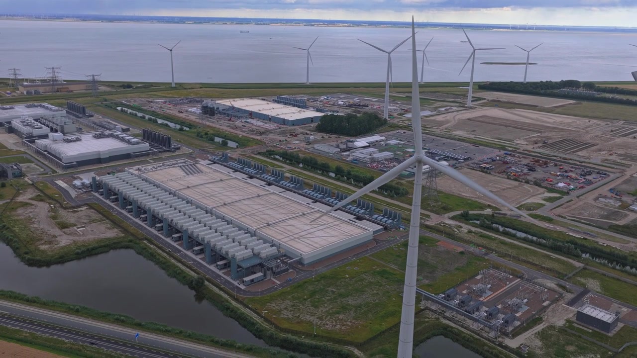 Aerial footage showing the vast google data center complex in eemshaven, netherlands, surrounded by large wind turbines producing renewable energy