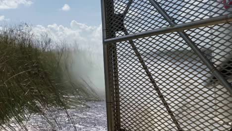 Slow-motion-close-up-shot-of-the-back-of-an-air-boat-traveling-through-the-Florida-everglades-near-Miami-leaving-a-wake-in-the-murky-water-surrounded-by-tall-grass-with-the-metal-cage-and-propeller