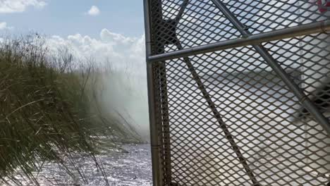 cámara lenta de cerca de la parte trasera de un barco de aire viajando a través de los everglades de florida cerca de miami dejando una estela en el agua turbia rodeada de hierba alta con la jaula de metal y la hélice