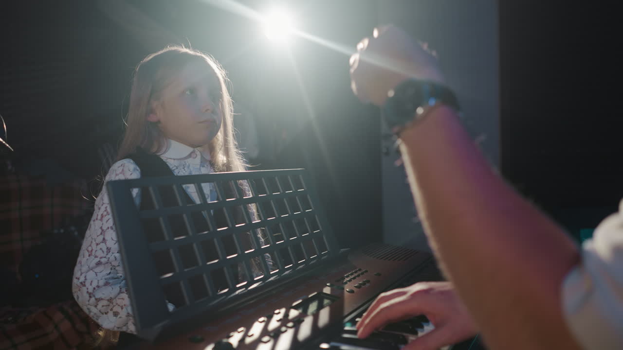 niño aprende a cantar con el maestro en el estudio de música. niña estudiante se entrena vocal con un músico tocando sintetizador en clase contra la luz de fondo. niño artístico