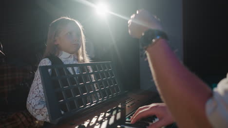 niño aprende a cantar con el maestro en el estudio de música. niña estudiante se entrena vocal con un músico tocando sintetizador en clase contra la luz de fondo. niño artístico