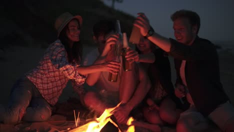 grupo de jóvenes brindando con botellas de cerveza y teniendo una fiesta en la playa en una noche de verano diciendo saludos con cerveza en 4k