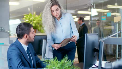 en la gran oficina la mujer de negocios entra en la oficina de vidrio y muestra la tableta a su colega. el edificio moderno de vidrio e hormigón está lleno de gente de negocios ocupada.