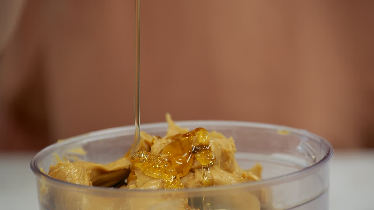 Adding honey to a peanut butter mixture in a blender