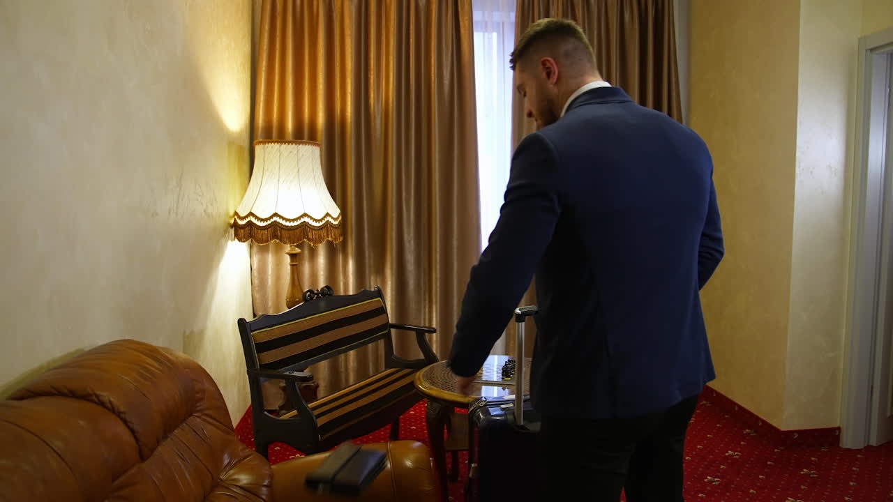 Handsome man comes into a hotel room. Elegant man taking off his costume jacket and opening curtains at hotel room. Slow motion. Back view.
