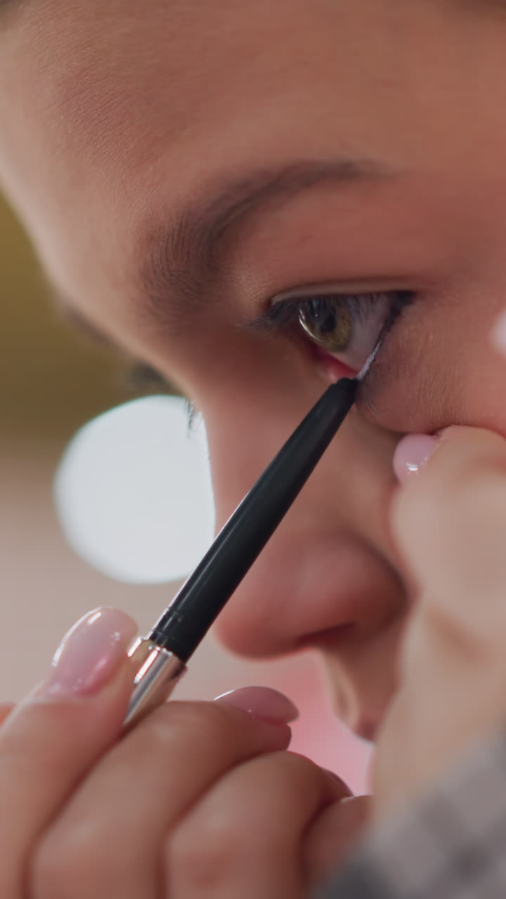 Youthful eye definition, Teen girl carefully tightlining with pencil near lash roots indoors, Young girl practices delicate upper waterline makeup with steady hand and soft lighting indoors