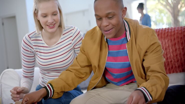 Happy diverse group of teenage friends sitting on couch and eating pizza at home, slow motion