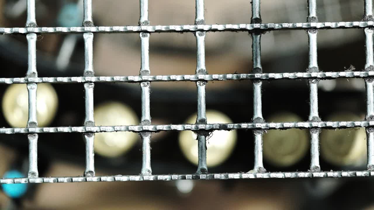 Cans in a factory moving under a metal grid as seen from above