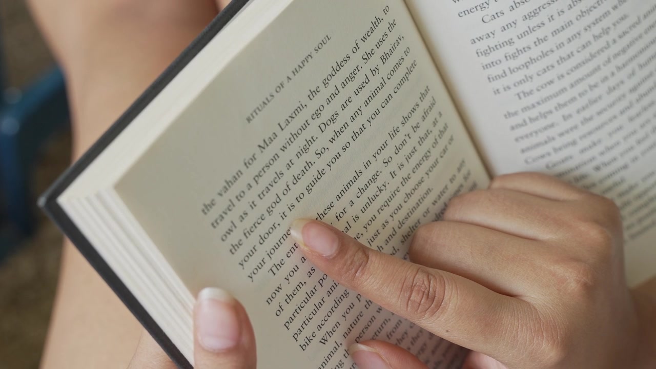 Close-up of a woman's hand gently pressing and smoothing an open book page while reading, with clearly visible printed text and soft natural window light illuminating.