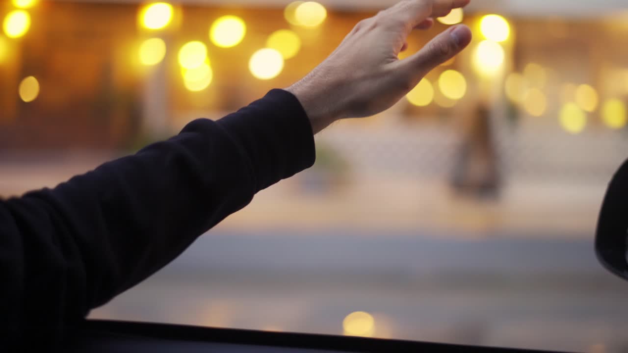 A man's hand is catching the wind while driving a car by street