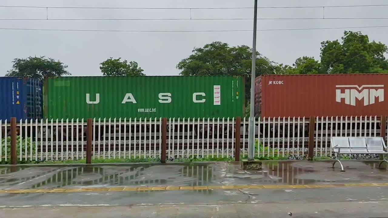 Passing by a train station in Indian village with vibrant freight train moving in background, rural transport and Indian railway life during monsoon season.