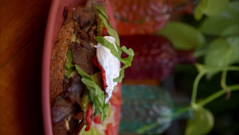 disparo vertical en cámara lenta de un sándwich de carne de res cubierto de rúcula mozzarella queso pepinillos pepino y tomate servido con ensalada