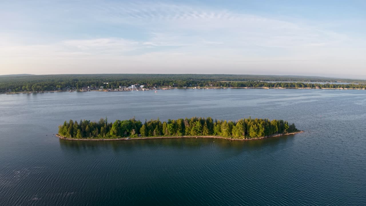 Aerial drone footage of a small forested island surrounded by calm blue waters in the Les Cheneaux Islands, Upper Peninsula of Michigan