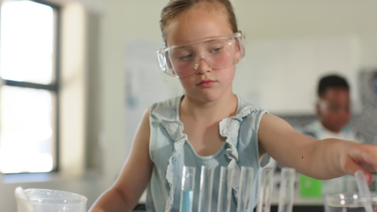 Pige, der udfører laboratorieopgave med at trække blå væske op med pipette og iføre sig beskyttelsesbriller ved laboratoriebordet