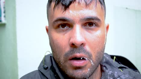el hombre escupe agua de la boca mientras lo lavan constantemente con una manguera