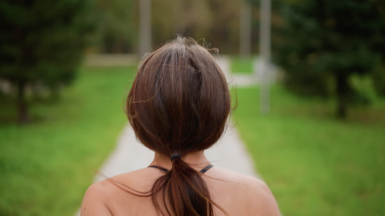 Back view of sporty woman in black top jogging through park with blurred green background, ideal for fitness, exercise, and outdoor running content showcasing athletic movement and health lifestyle