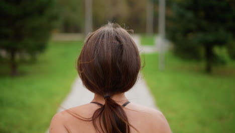 back view of sporty woman in black top jogging through park with blurred green background, ideal for fitness, exercise, and outdoor running content showcasing athletic movement and health lifestyle